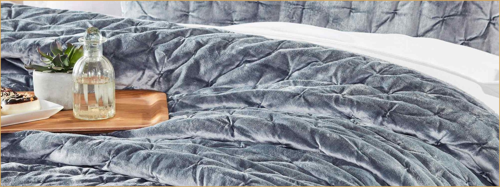 Wide banner image of a velvet quilt on a bed, styled with decor on a wooden tray.